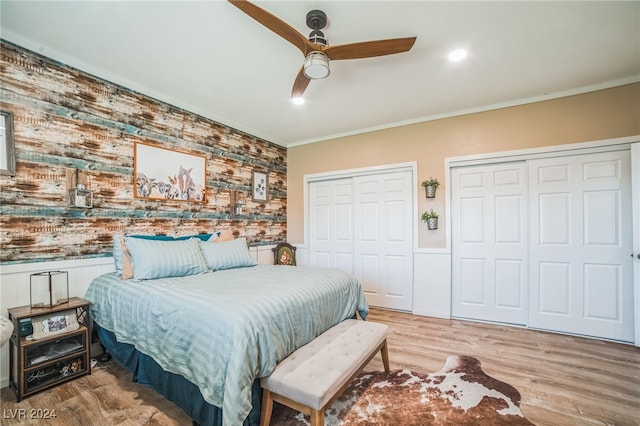 bedroom featuring multiple closets, ceiling fan, light hardwood / wood-style flooring, and crown molding