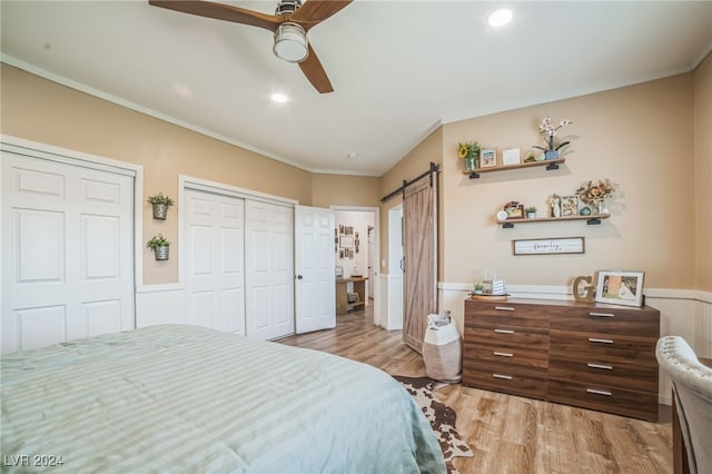 bedroom with light wood-type flooring, ornamental molding, ceiling fan, a barn door, and multiple closets