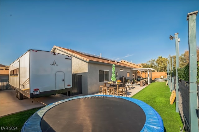 rear view of property featuring a trampoline, a patio area, and a lawn