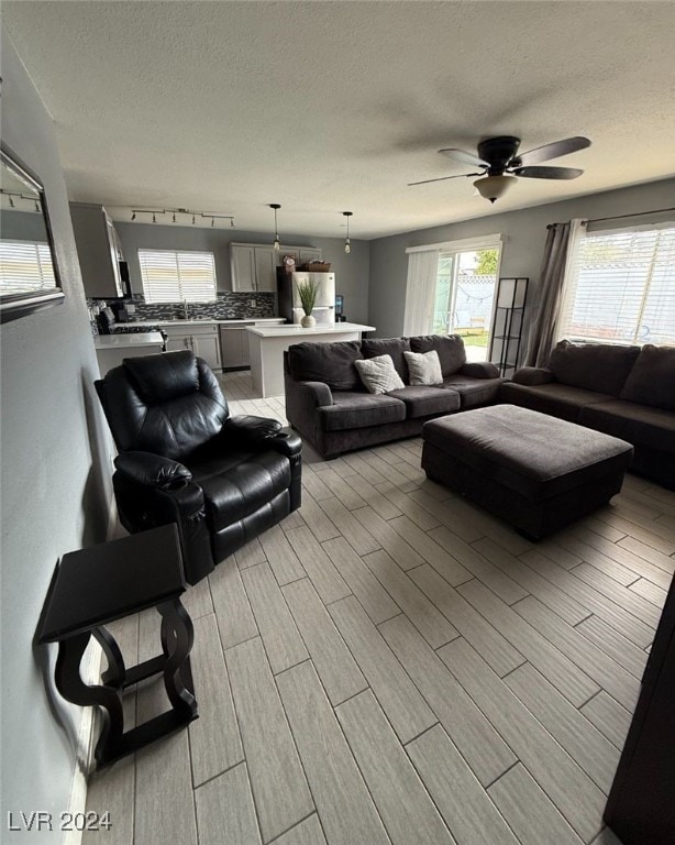 living room featuring ceiling fan, rail lighting, a textured ceiling, and light wood-type flooring