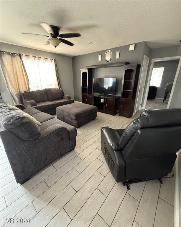 living room featuring ceiling fan, light wood-type flooring, and a textured ceiling