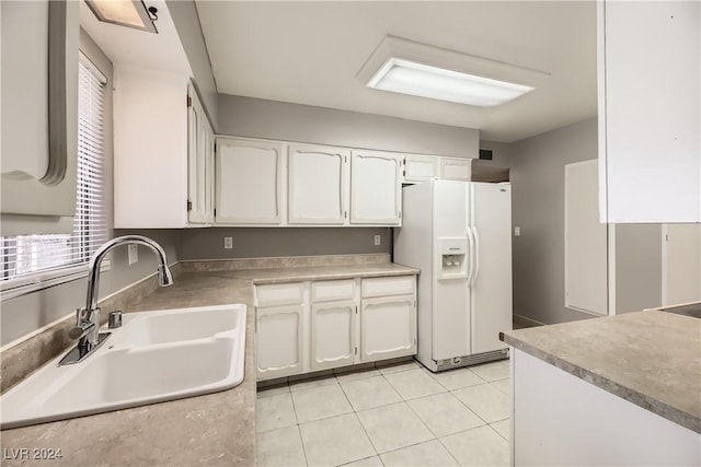 kitchen with white refrigerator with ice dispenser, light tile patterned floors, white cabinetry, and sink