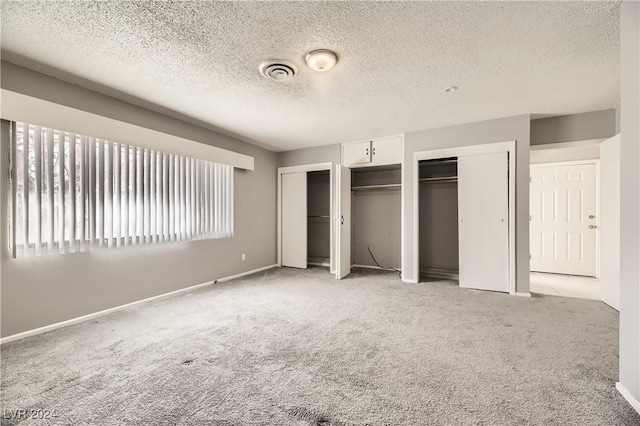 unfurnished bedroom featuring light colored carpet, a textured ceiling, and multiple closets