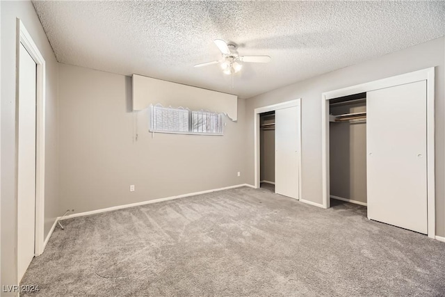 unfurnished bedroom with ceiling fan, light colored carpet, a textured ceiling, and multiple closets