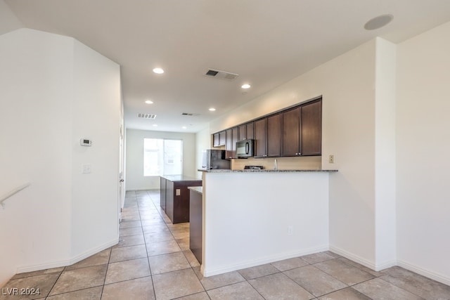 kitchen with black refrigerator, kitchen peninsula, light stone counters, dark brown cabinets, and light tile patterned floors