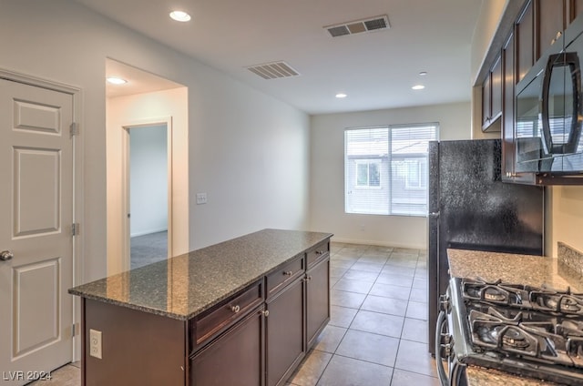 kitchen featuring a center island, dark stone countertops, light tile patterned flooring, dark brown cabinetry, and gas stove