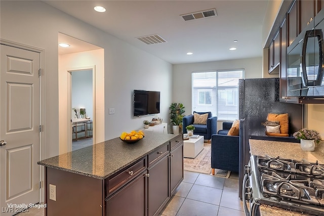 kitchen featuring dark brown cabinets, light tile patterned floors, dark stone counters, and stainless steel range with gas stovetop