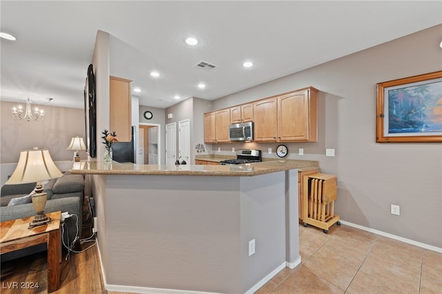 kitchen with kitchen peninsula, light stone counters, stainless steel appliances, light brown cabinets, and a notable chandelier