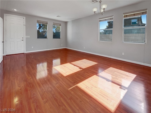 unfurnished room featuring plenty of natural light, wood-type flooring, and an inviting chandelier