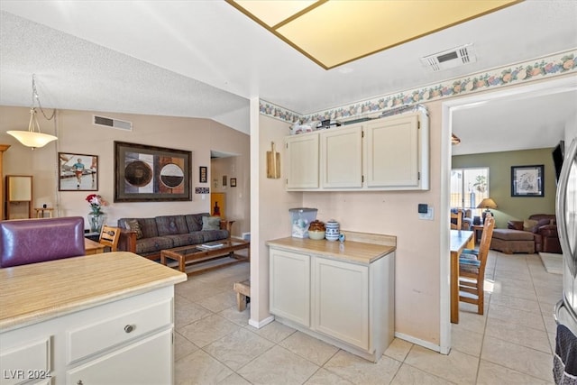 kitchen featuring a textured ceiling, vaulted ceiling, light tile patterned floors, decorative light fixtures, and white cabinetry