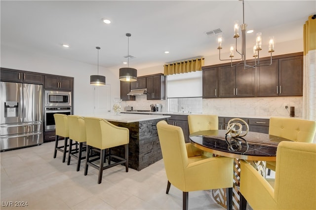 kitchen with appliances with stainless steel finishes, tasteful backsplash, dark brown cabinetry, a kitchen island, and hanging light fixtures