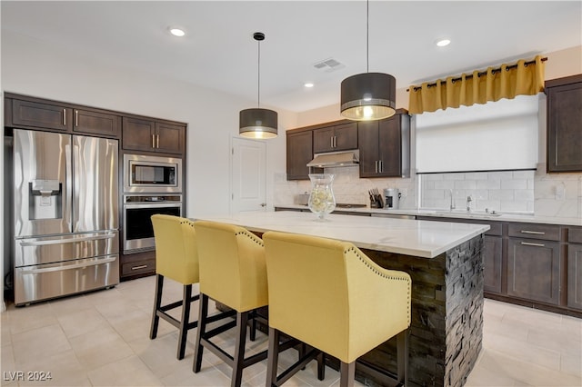 kitchen featuring decorative light fixtures, a kitchen island, a kitchen bar, and stainless steel appliances