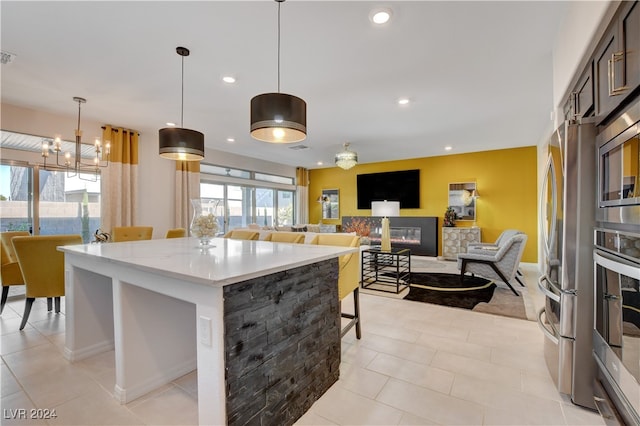 kitchen featuring a center island, hanging light fixtures, a kitchen breakfast bar, a stone fireplace, and light stone counters