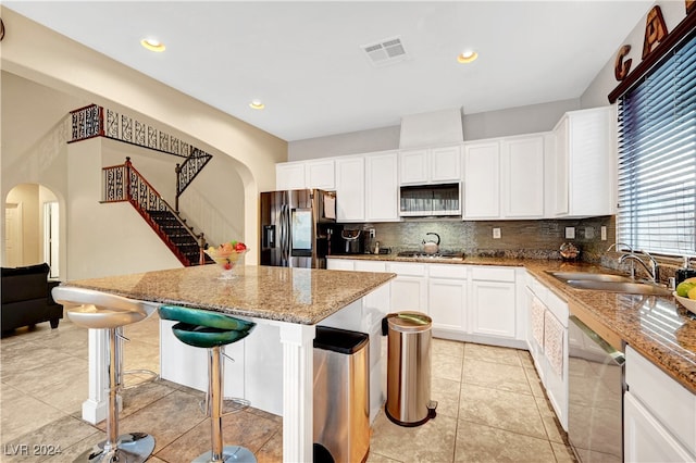 kitchen with light stone countertops, a kitchen island, a kitchen breakfast bar, white cabinets, and appliances with stainless steel finishes