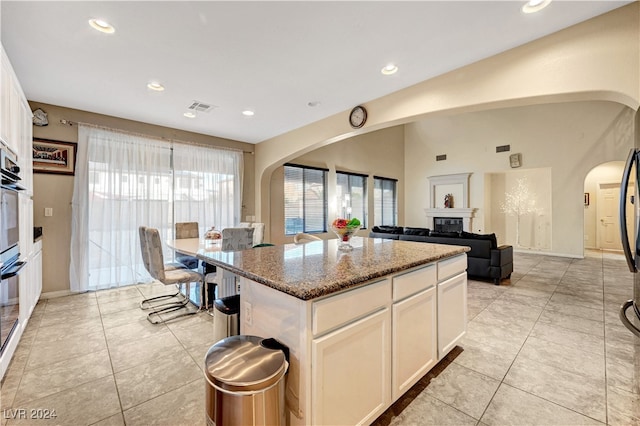 kitchen featuring a kitchen island, light tile patterned floors, light stone countertops, and white cabinetry