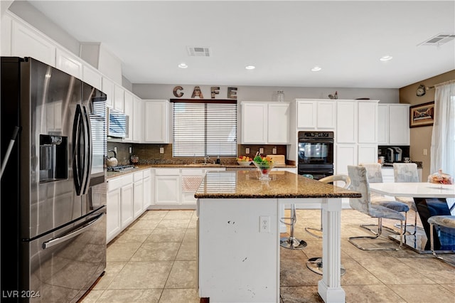 kitchen with light tile patterned floors, a kitchen island, dark stone counters, white cabinets, and appliances with stainless steel finishes