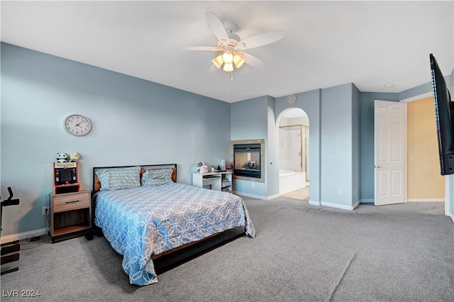 bedroom featuring a multi sided fireplace, connected bathroom, light colored carpet, and ceiling fan