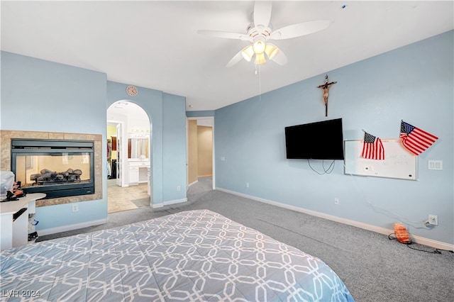 carpeted bedroom with a multi sided fireplace, connected bathroom, and ceiling fan