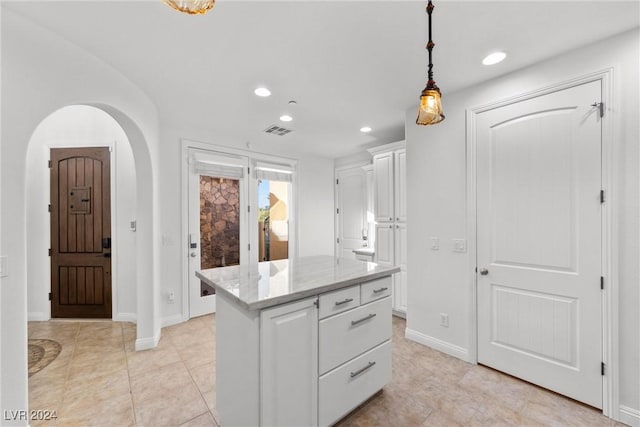 kitchen with white cabinets, light stone countertops, light tile patterned floors, decorative light fixtures, and a kitchen island