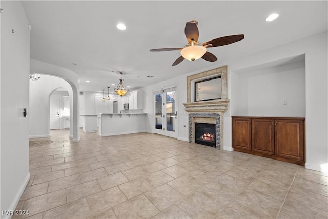 unfurnished living room with ceiling fan, light tile patterned flooring, and a stone fireplace