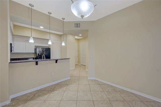 kitchen with a kitchen bar, white cabinetry, black fridge, hanging light fixtures, and light tile patterned floors