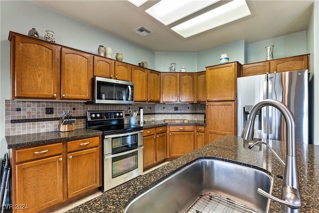 kitchen featuring sink, stainless steel appliances, dark stone counters, and tasteful backsplash