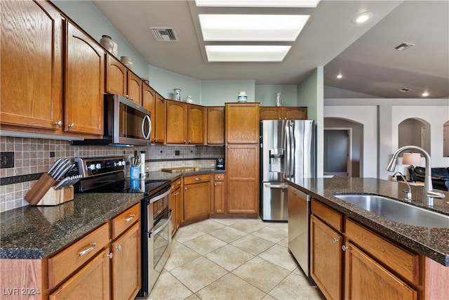 kitchen with sink, dark stone countertops, tasteful backsplash, light tile patterned flooring, and stainless steel appliances