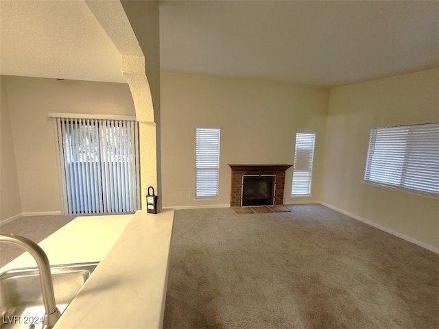 unfurnished living room featuring carpet, sink, and a brick fireplace