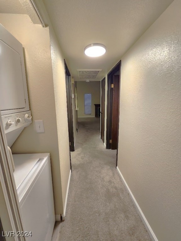 washroom featuring light colored carpet and stacked washer / dryer