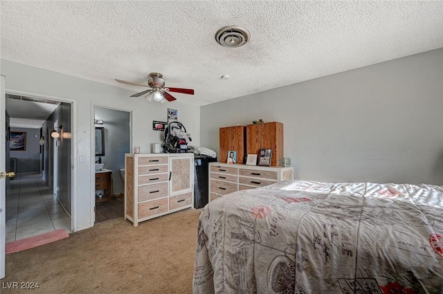 bedroom featuring a textured ceiling, carpet floors, ensuite bath, and ceiling fan