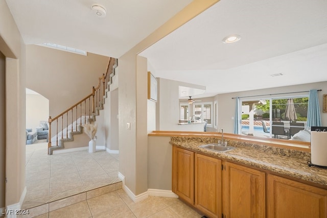 kitchen featuring light tile patterned flooring, light stone counters, ceiling fan, and sink