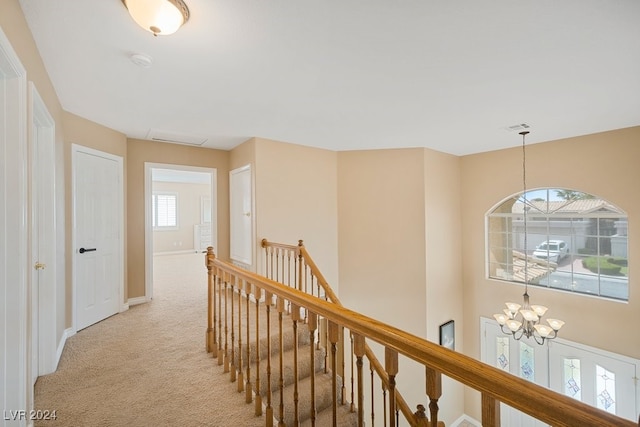 hallway featuring light carpet, a healthy amount of sunlight, and an inviting chandelier