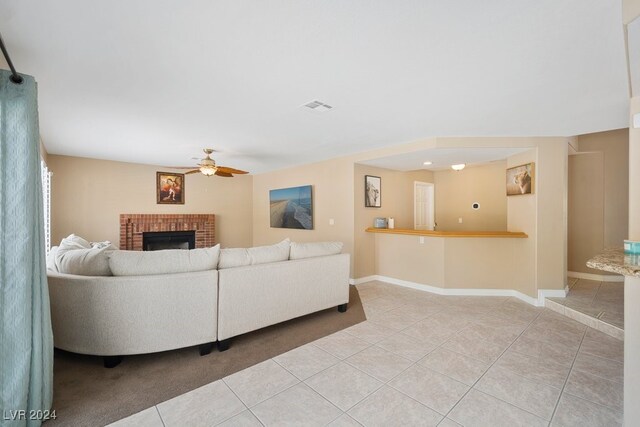 tiled living room featuring ceiling fan and a brick fireplace