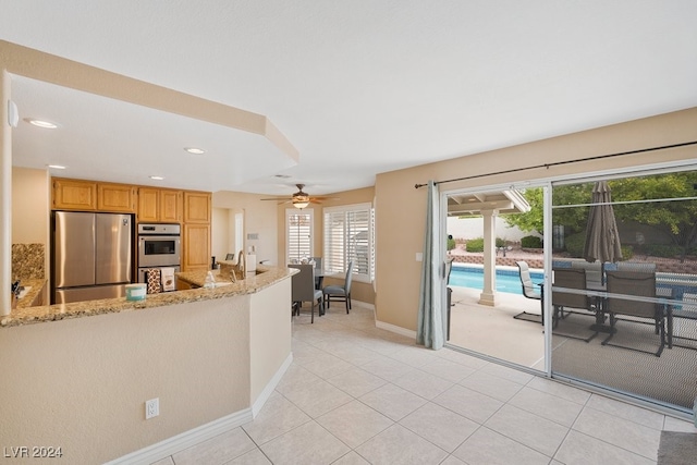 kitchen with kitchen peninsula, light stone counters, stainless steel appliances, ceiling fan, and light tile patterned floors