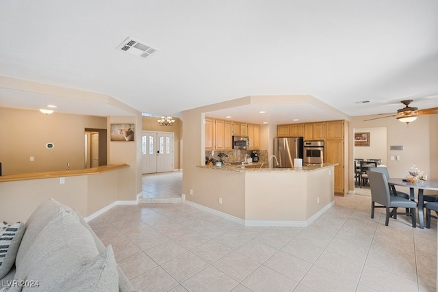 kitchen featuring light stone countertops, backsplash, kitchen peninsula, light brown cabinetry, and appliances with stainless steel finishes