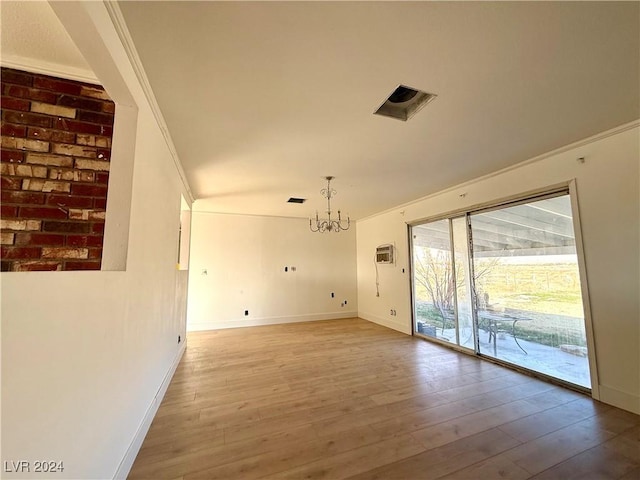 unfurnished living room with light hardwood / wood-style floors, ornamental molding, a wall mounted AC, and a chandelier