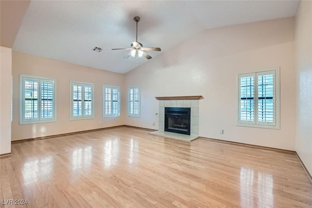 unfurnished living room featuring light hardwood / wood-style floors, high vaulted ceiling, ceiling fan, and a tiled fireplace