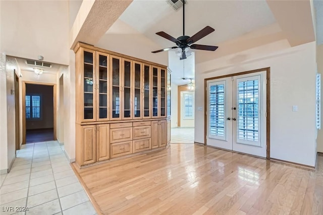 unfurnished living room with ceiling fan, light hardwood / wood-style floors, high vaulted ceiling, and french doors