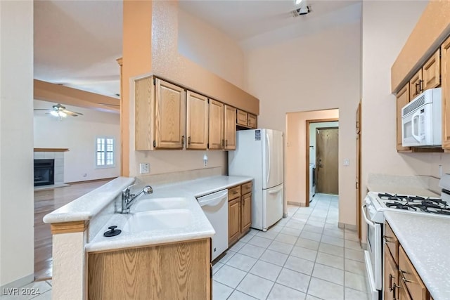 kitchen with white appliances, ceiling fan, a fireplace, light tile patterned flooring, and kitchen peninsula