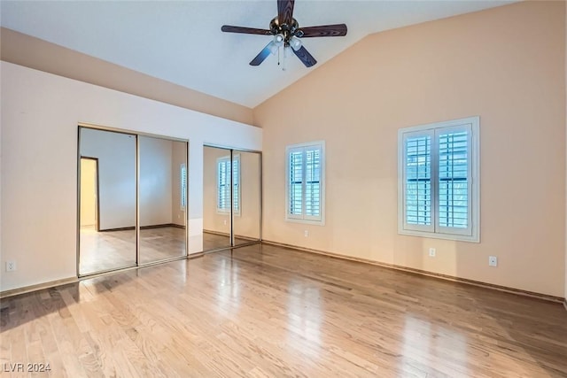 unfurnished bedroom with ceiling fan, light hardwood / wood-style floors, high vaulted ceiling, and multiple closets