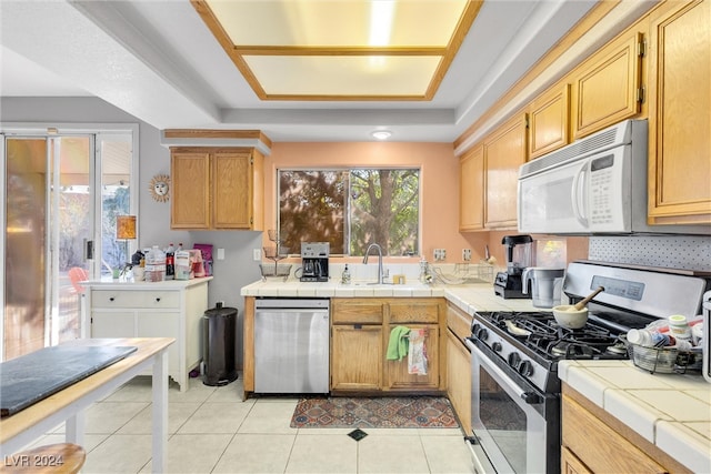 kitchen featuring tile countertops, a raised ceiling, sink, light tile patterned floors, and stainless steel appliances