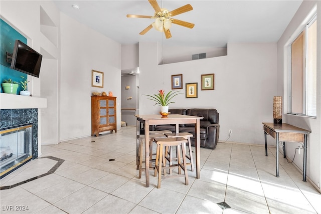 dining space with ceiling fan, light tile patterned floors, high vaulted ceiling, and a tiled fireplace