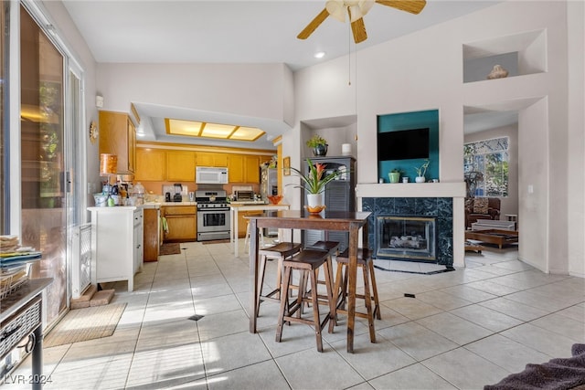 kitchen with gas range, ceiling fan, high vaulted ceiling, a fireplace, and light tile patterned flooring