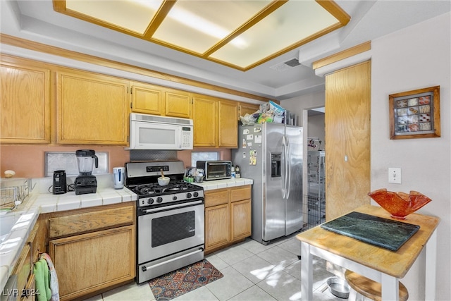 kitchen with a tray ceiling, tile counters, light tile patterned floors, and stainless steel appliances