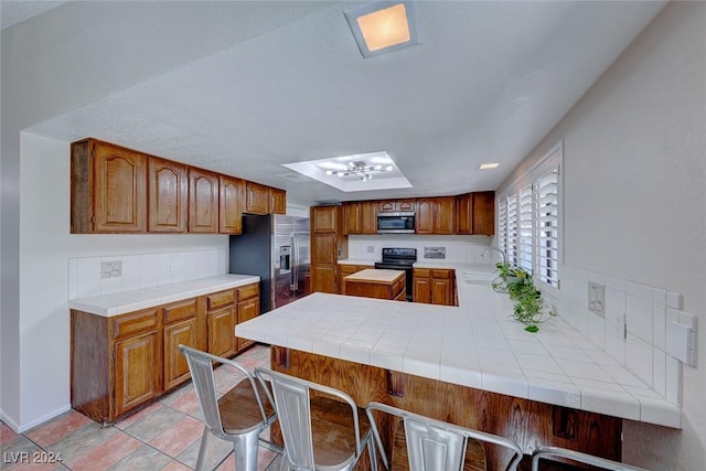 kitchen featuring tile countertops, sink, appliances with stainless steel finishes, a kitchen bar, and kitchen peninsula