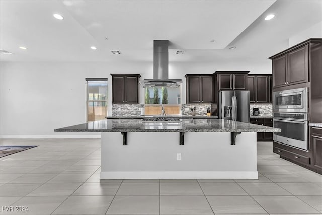 kitchen featuring a large island, a kitchen breakfast bar, island exhaust hood, dark stone countertops, and appliances with stainless steel finishes