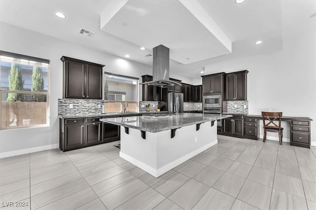 kitchen featuring a kitchen breakfast bar, decorative backsplash, a kitchen island, island exhaust hood, and stainless steel appliances