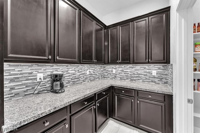 kitchen with dark brown cabinetry, light stone counters, and backsplash