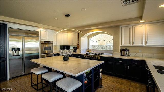 kitchen with appliances with stainless steel finishes, light stone counters, decorative light fixtures, white cabinets, and a center island