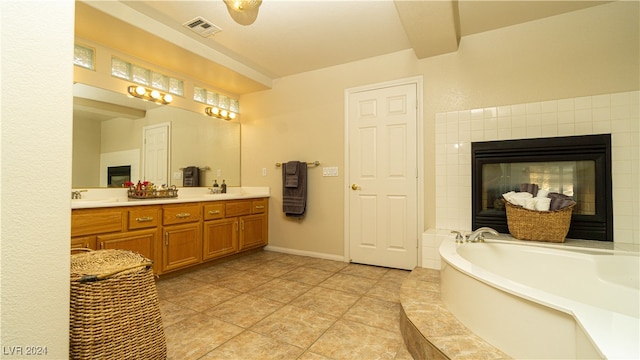 bathroom featuring tile patterned flooring, vanity, a fireplace, and tiled tub